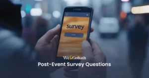 The Best Post-Event Survey Questions for Event Feedback A close-up shows a person holding a smartphone with the "We & Goliath Post-Event Survey Questions" interface on display. The urban backdrop is softly blurred, keeping focus on the screen's details.