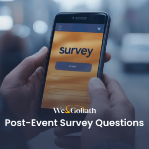 A close-up shows a person holding a smartphone with the "We & Goliath Post-Event Survey Questions" interface on display. The urban backdrop is softly blurred, keeping focus on the screen's details.