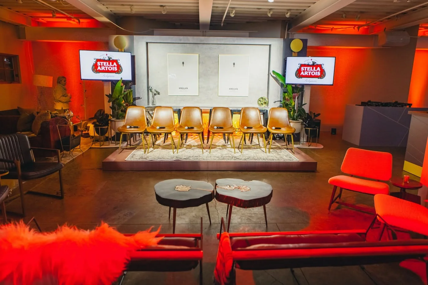 Empty event venue lit in red with a stage and lounge seating
