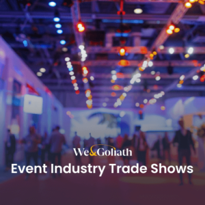 Attendees at a busy event industry trade show with exhibition stands and lighting in the background.