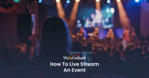 How to Effectively Stream Your Events Online A person operating a live stream of an event with a laptop, viewed from behind with the stage in the background.