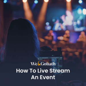 How to Effectively Stream Your Events Online A person operating a live stream of an event with a laptop, viewed from behind with the stage in the background.