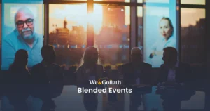 Blended Events: The Future of Event Planning Group of professionals in a meeting at dusk with digital presentations in the background, featuring the text "we&goliath blended events.