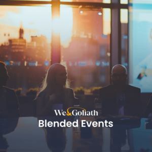 Blended Events: The Future of Event Planning Group of professionals in a meeting at dusk with digital presentations in the background, featuring the text "we&goliath blended events.