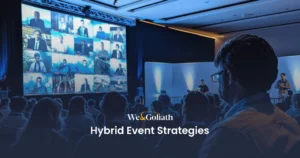 Hybrid Event Strategies: Bridging the Gap with Virtual Events Audience at a hybrid event viewing multiple virtual speakers displayed on a large screen, with the text "webgoliath hybrid event strategies" overlaying the image.