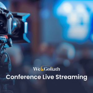 Best Practices for Live Streaming Your Conference A video camera is set up to live stream a conference, with a blurred audience and presenter in the background, and the text "We & Goliath Conference Live Streaming" displayed at the bottom.