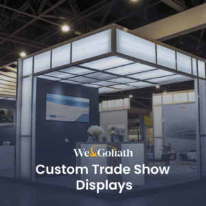 A trade show booth featuring a modern design with illuminated displays, monitors, and banners, showcasing "We & Goliath: Custom Trade Show Displays.