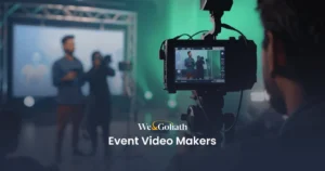 Create Event Promo Videos Online for Free A camera records two speakers on stage at an event. Text overlay reads "We&Goliath Event Video Makers.