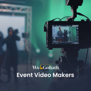 Create Event Promo Videos Online for Free A camera records two speakers on stage at an event. Text overlay reads "We&Goliath Event Video Makers.