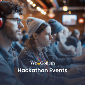 Hackathon Guide: Tech Events You Can't Miss People working on laptops at a hackathon event in a spacious indoor venue; one individual is wearing red headphones. Text on image: "We & Goliath Hackathon Events.