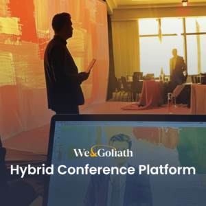 People are attending a conference; one speaker stands on stage holding a paper, another person sits in front of a laptop displaying the We & Goliath logo and "Hybrid Conference Platform" text.