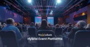 Host Your Next Hybrid Event with These Top Platforms A large audience seated in a conference hall, facing a stage with a presentation screen. Text on the image reads "We & Goliath Hybrid Event Platforms.