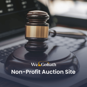 A judge's gavel resting on a laptop keyboard with the text "We & Goliath Non-Profit Auction Site" displayed at the bottom.