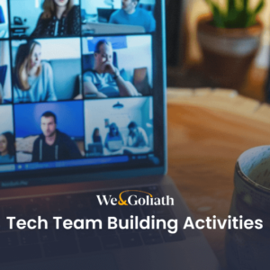 Tech Team Building Activities: Uniting Virtual Teams at Work A laptop screen shows a video call with multiple participants. Text on the image reads, "We & Goliath Tech Team Building Activities." A mug sits on the table in front of the laptop.