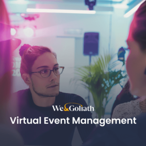 People engaged in conversation at an event, with a "We&Goliath Virtual Event Management" sign.