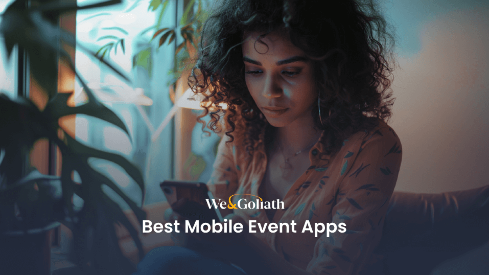 A person sits indoors, focused on their mobile phone. Text on the image reads, "We&Goliath Best Mobile Event Apps.