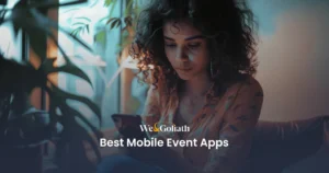 Comprehensive Guide to Mobile Event Applications A person sits indoors, focused on their mobile phone. Text on the image reads, "We&Goliath Best Mobile Event Apps.