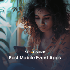 A person sits indoors, focused on their mobile phone. Text on the image reads, "We&Goliath Best Mobile Event Apps.