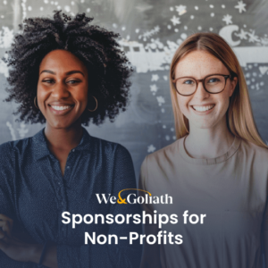 A diverse group of four smiling people stands in front of a chalkboard. A text overlay reads, "We & Goliath Sponsorships for Non-Profits.
