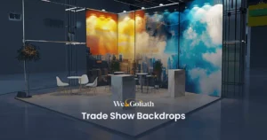 Trade Show Backdrops: Enhance Your Booth Display A modern exhibition booth with vibrant cityscape and cloud murals, featuring minimalist furniture including tables, chairs, and podiums, and two potted plants, set in an industrial hall.